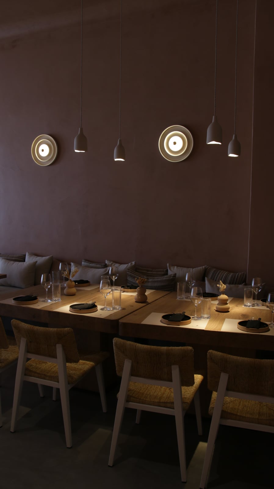 Round sconces and small ceramic pendants over set timber tables and a cushioned banquette at Bouboulo.