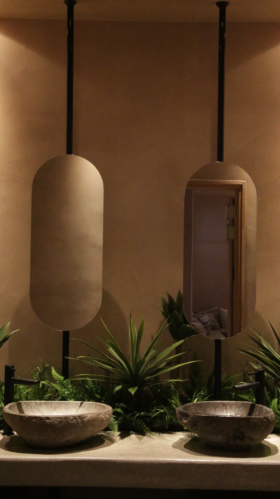 Two stone basins set in planting beneath oval mirrors hung on black rods in the Bouboulo washroom.