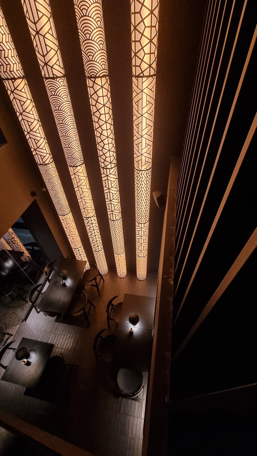 The patterned light columns at Koyasan seen from the upper floor, running down to dark tables and small lamps below.