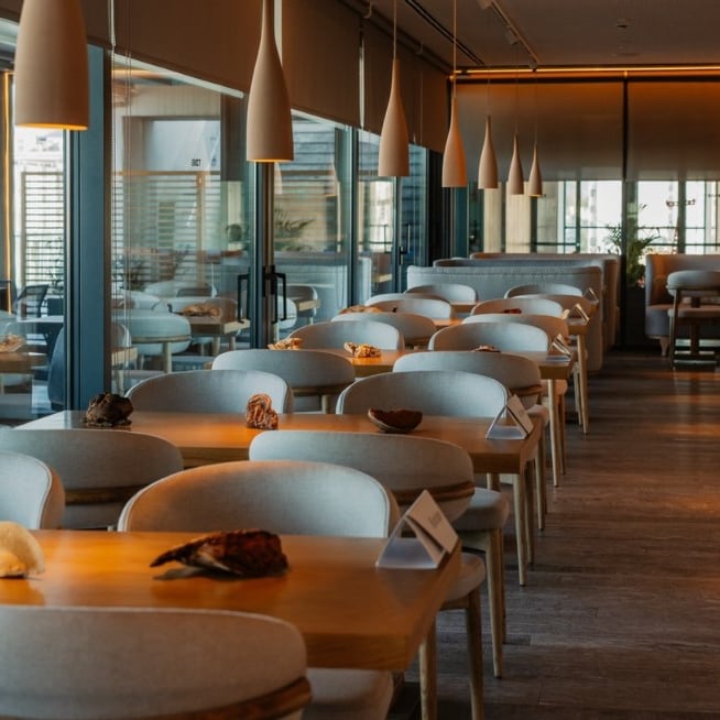The Nyn Esti dining room: slender pendants in a line over rows of timber tables, a warm line of light along the ceiling.