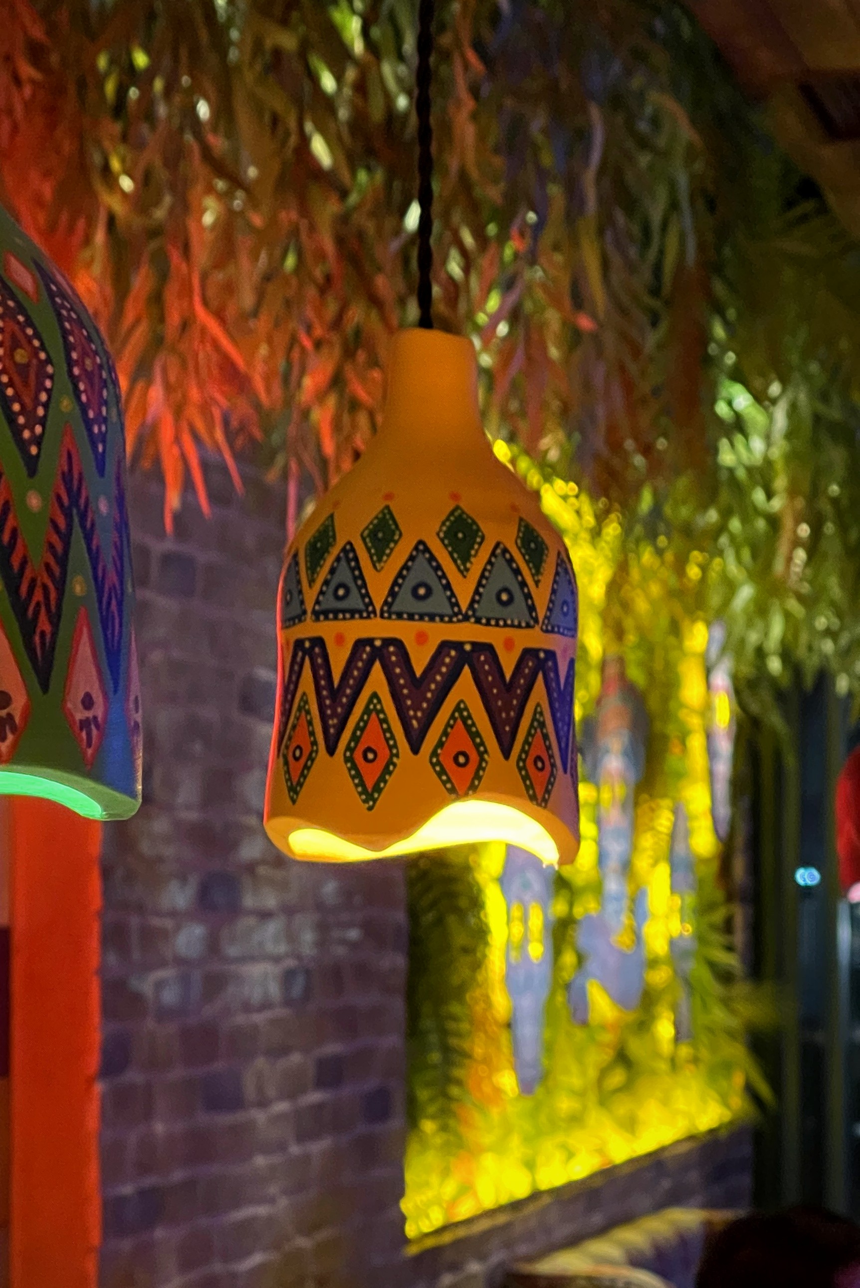 Two painted pendants beneath hanging foliage beside a planted wall lit green and gold at Panchito.