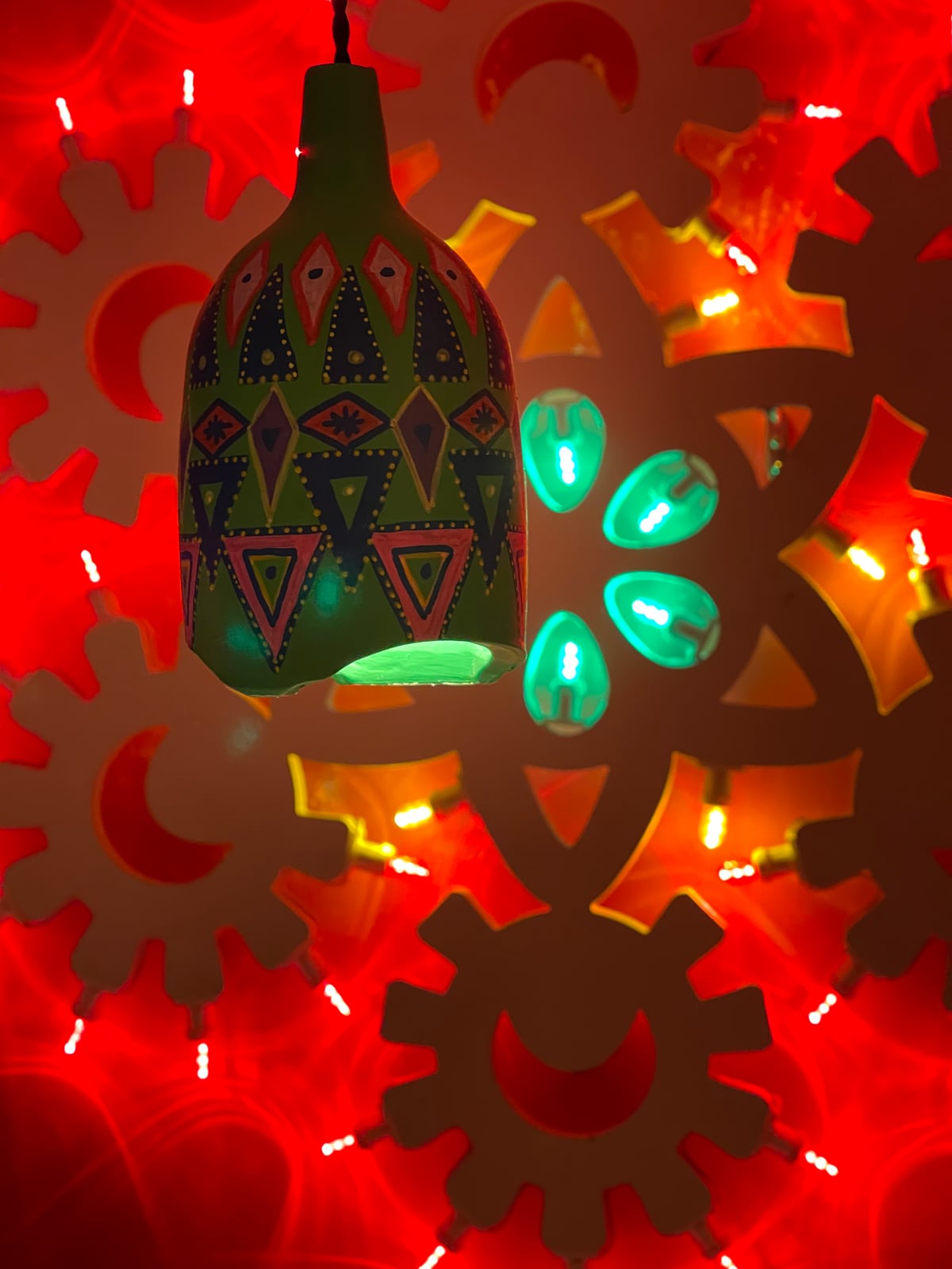 A hand painted pendant before a red wall of cut out gears at Panchito, lit from behind in red with turquoise petals at its centre.