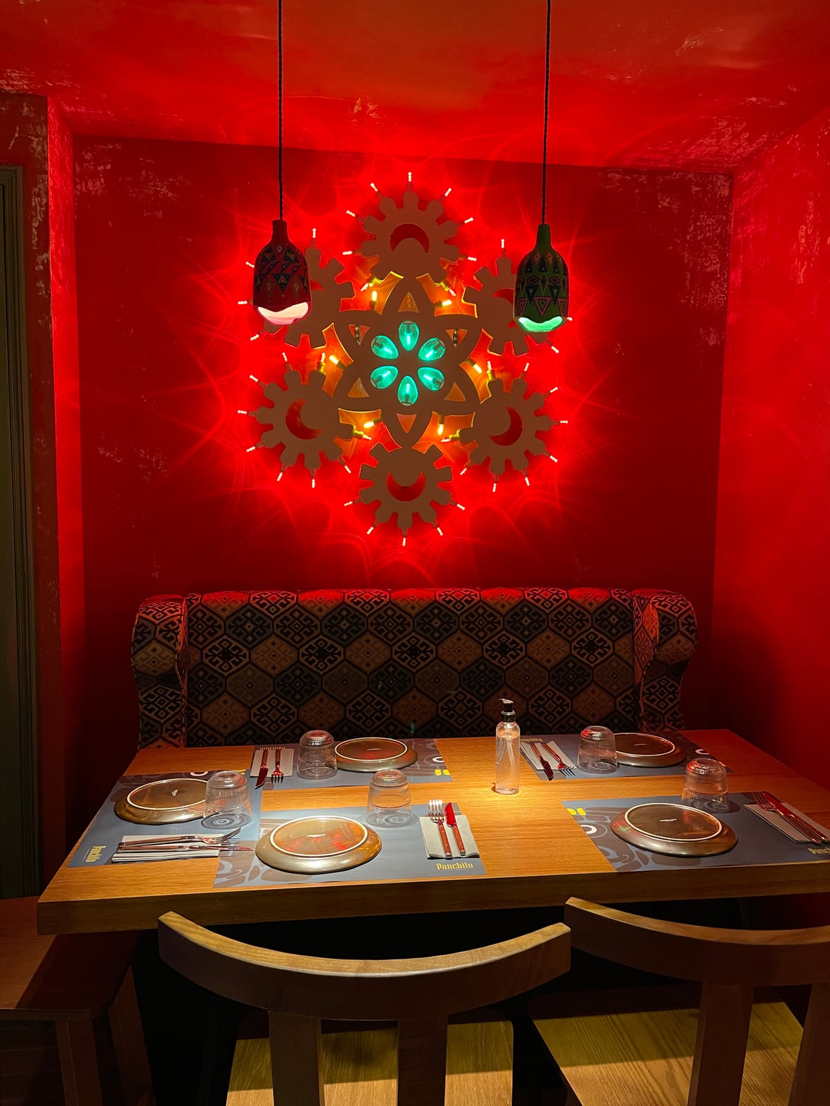 A table for four in a red booth at Panchito, two painted pendants above it and a cut out pattern glowing on the wall behind.