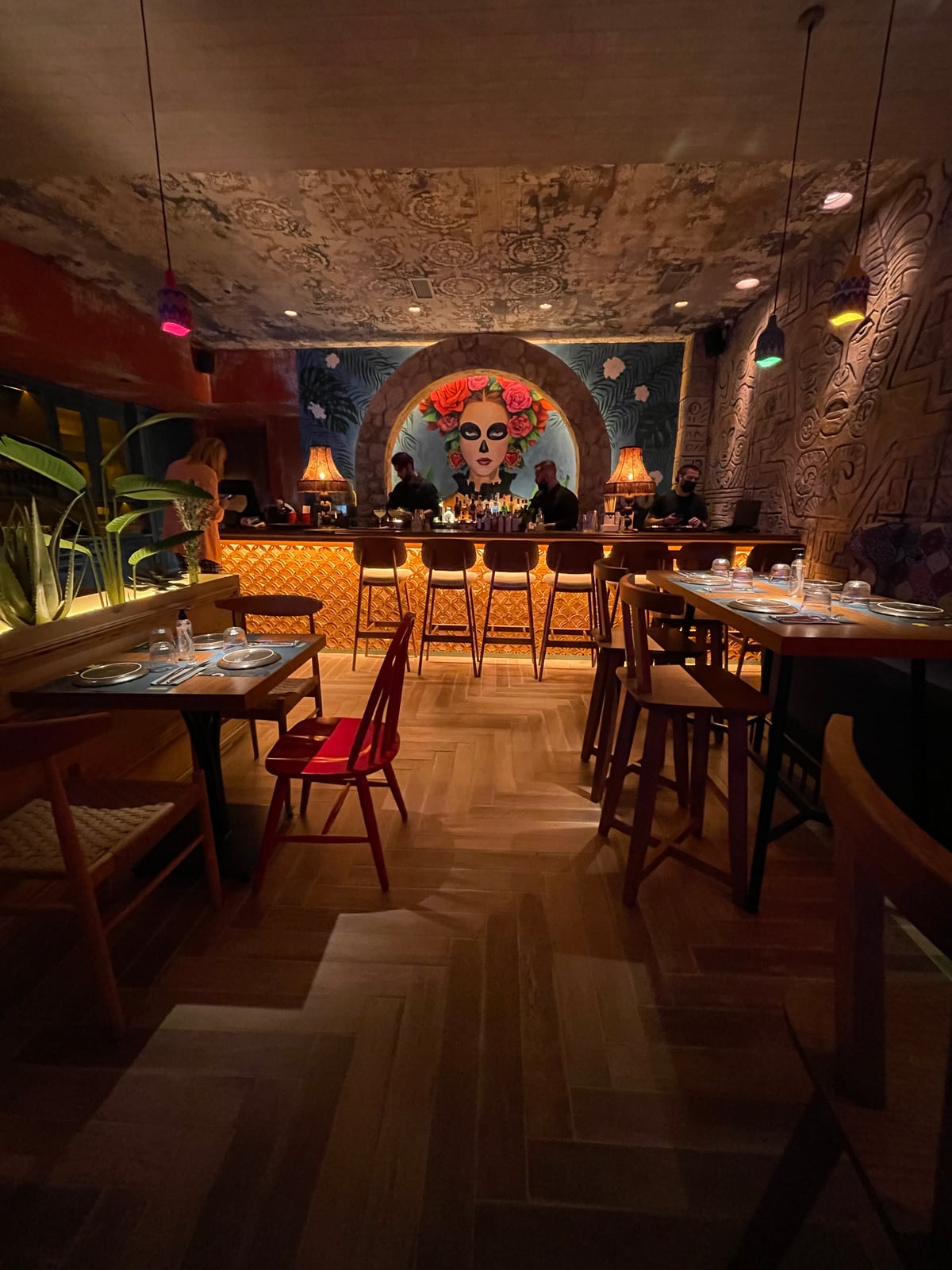 The Panchito dining room: tables and a red chair along a patterned wall, leading to the bar beneath a painted portrait in an arch.