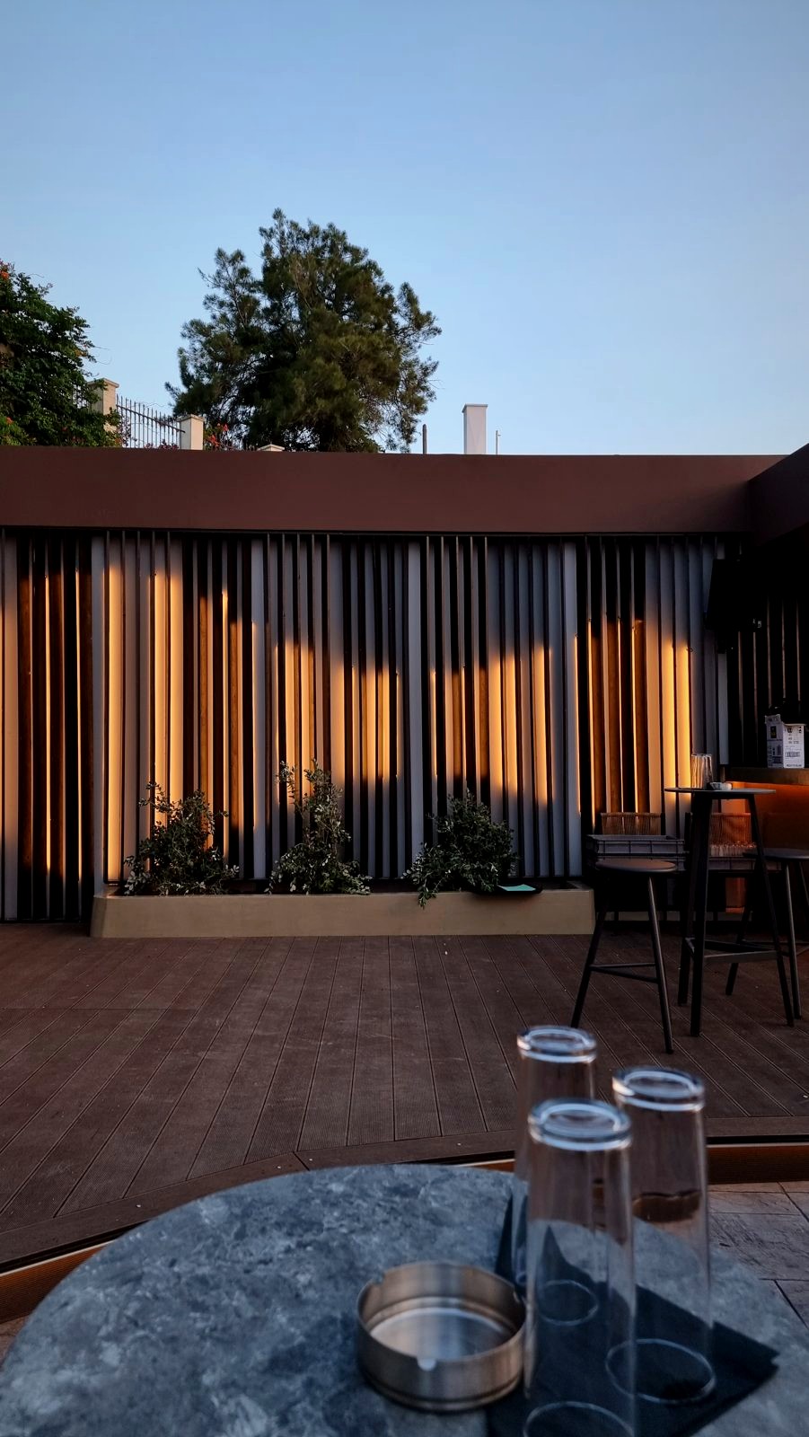 The Raval rooftop bar at dusk, its curtains lit from behind, a stone table with glasses in the foreground.