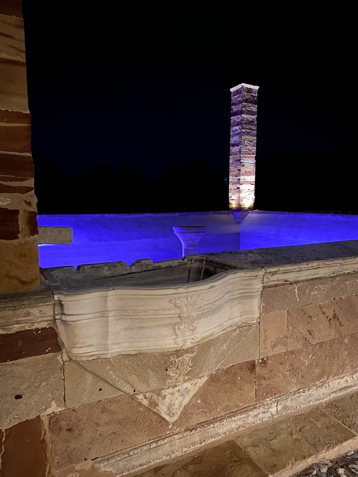 The stone edge of the villa's pool lit blue, a banded column beyond.
